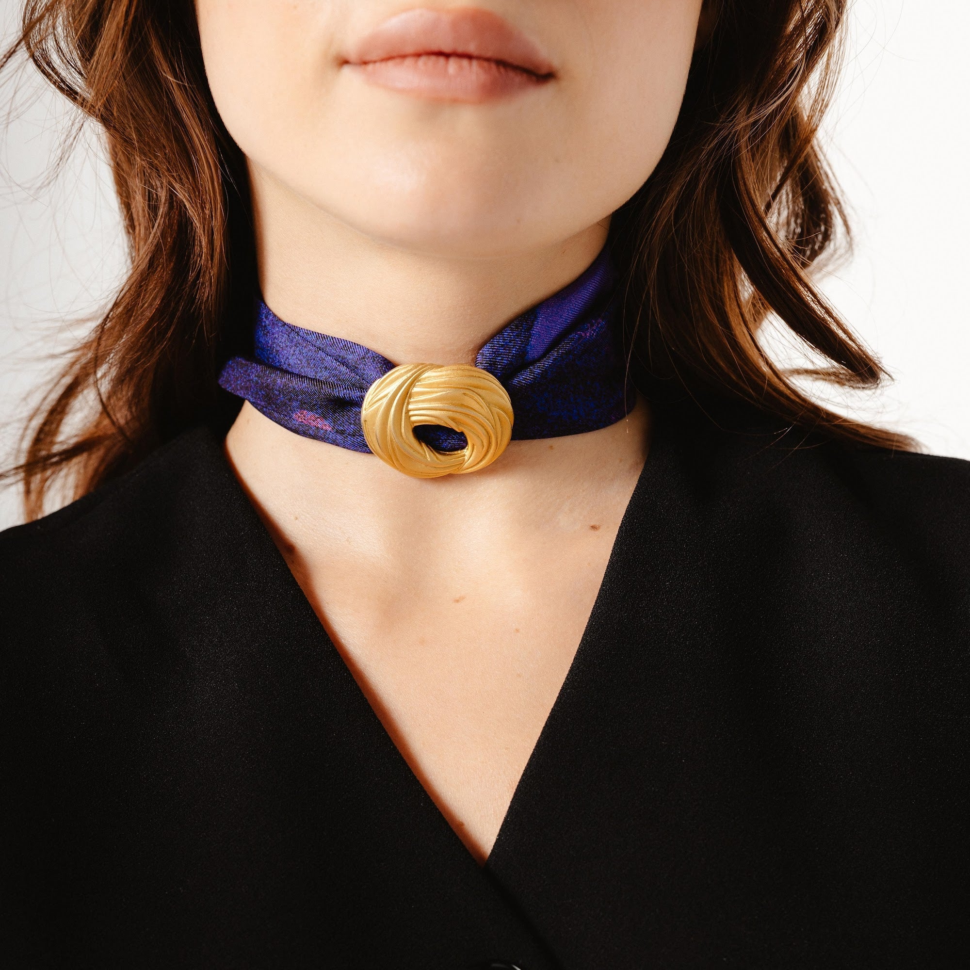 Purple print twilly scarf tied around neck with gold brooch