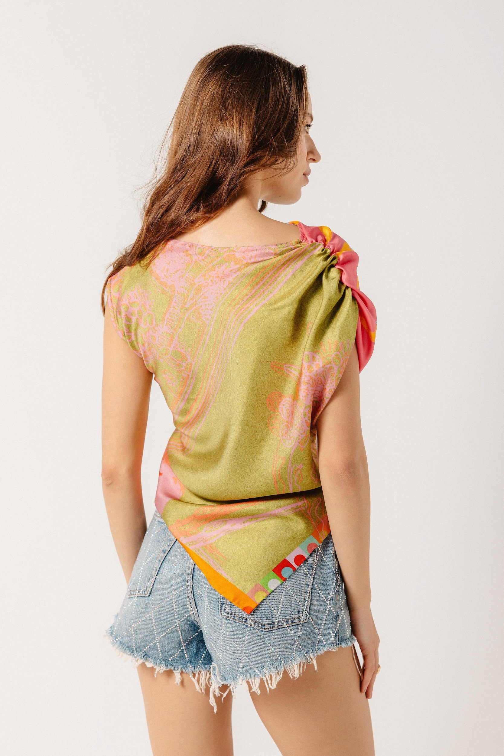 Model wearing asymmetrical silk top with green and pink print on back