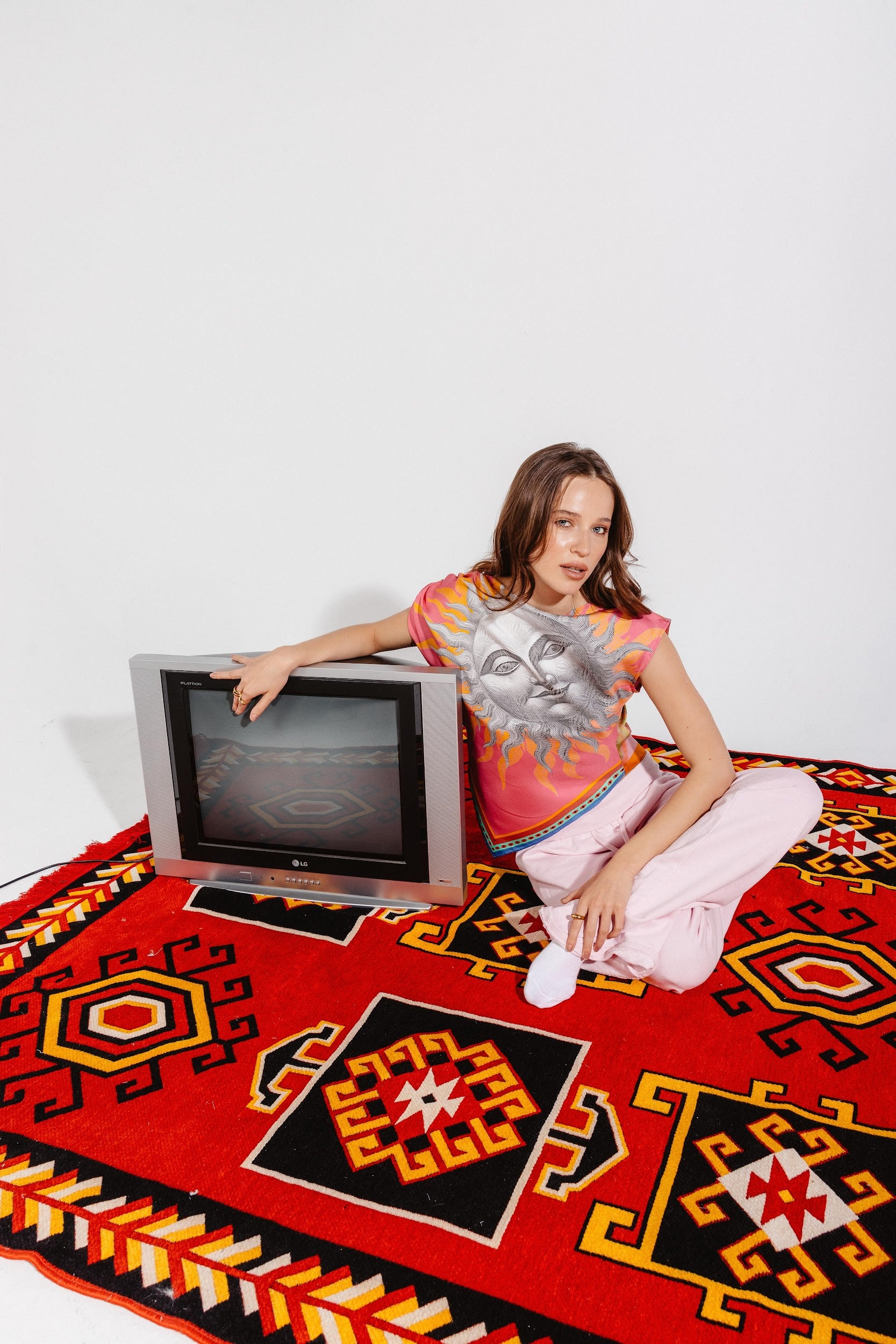 Model sitting next to TV wearing sun print top in silk