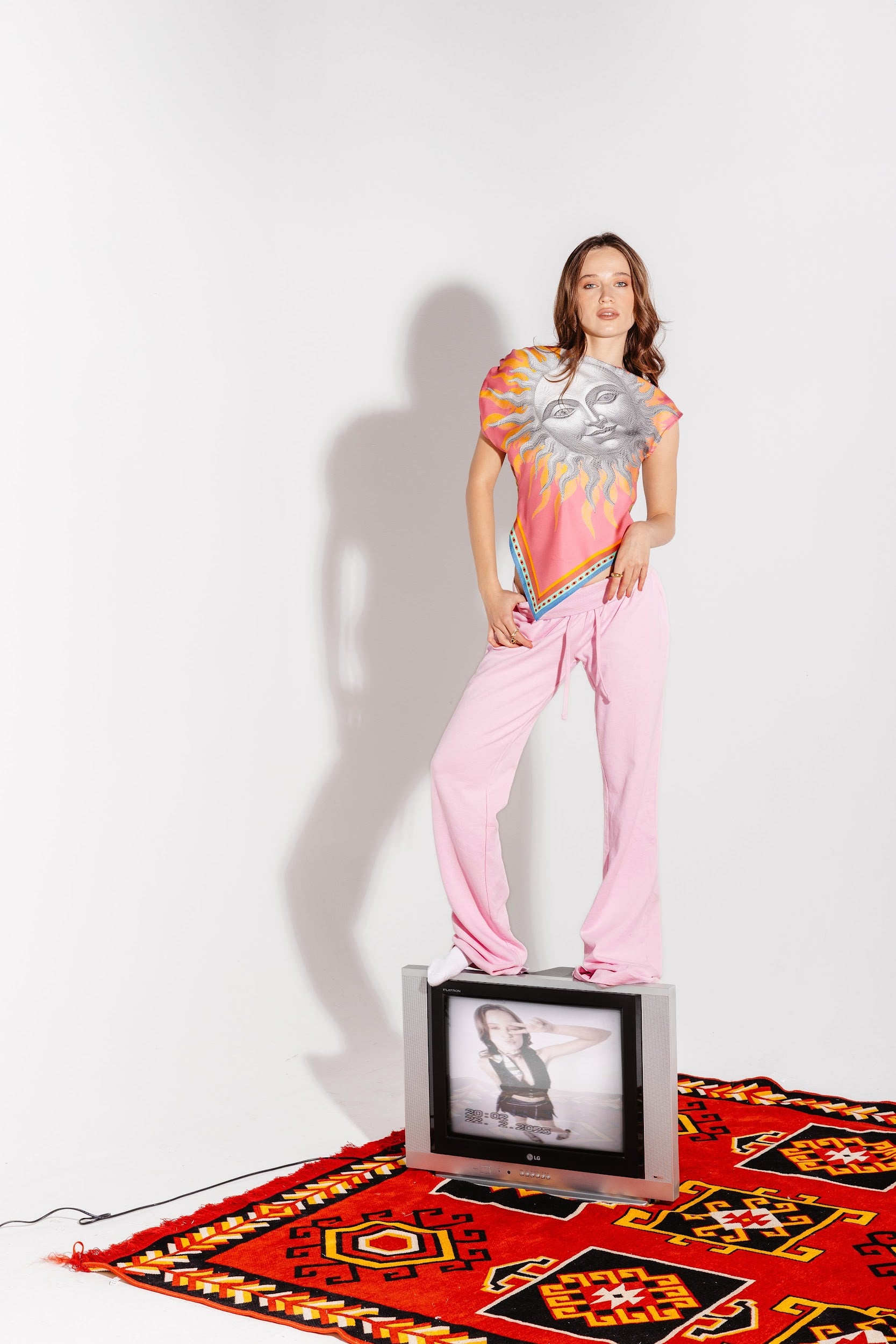 Model standing on TV wearing asymmetrical silk top with sun design