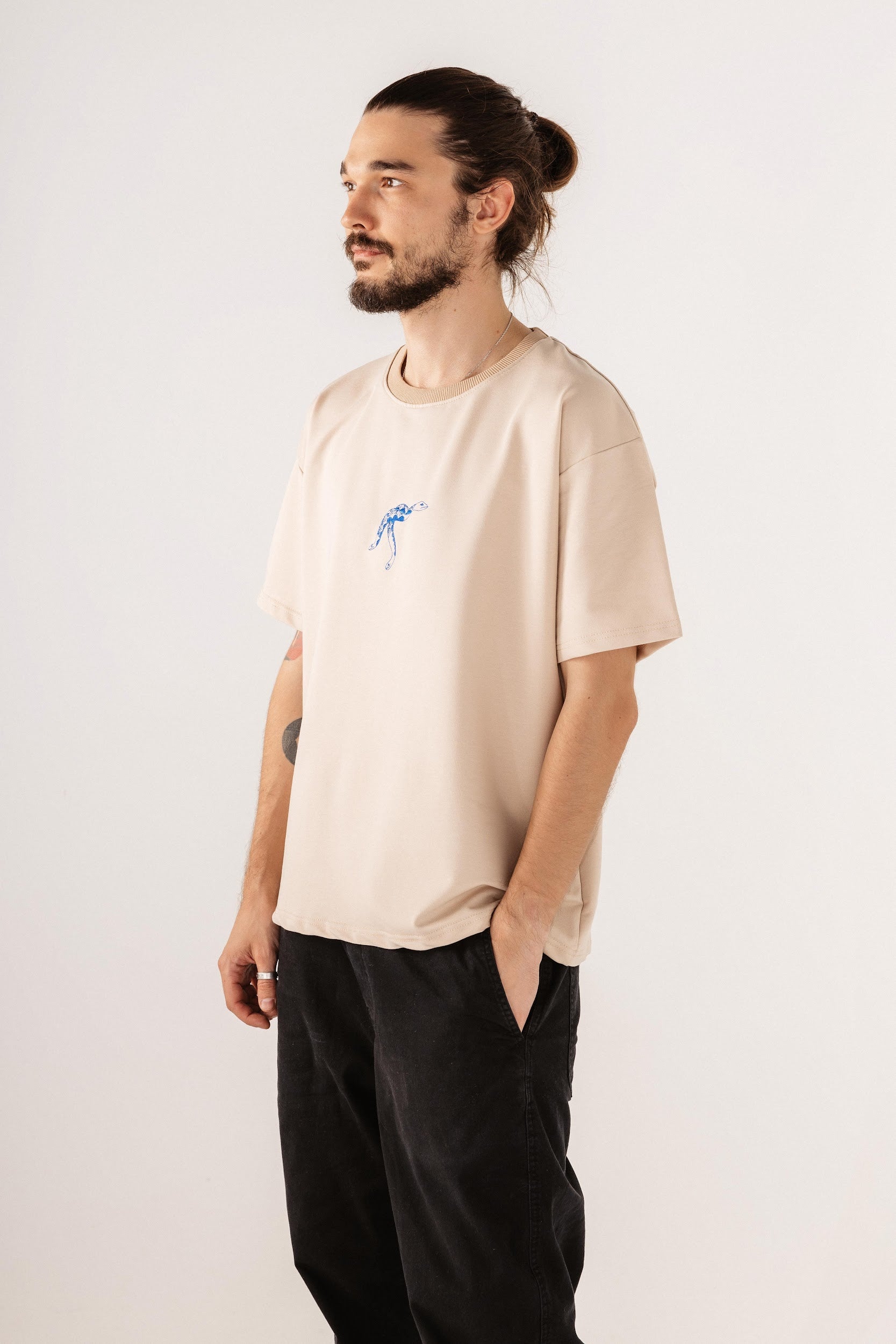 Male model wearing beige top with blue snake embroidery in front