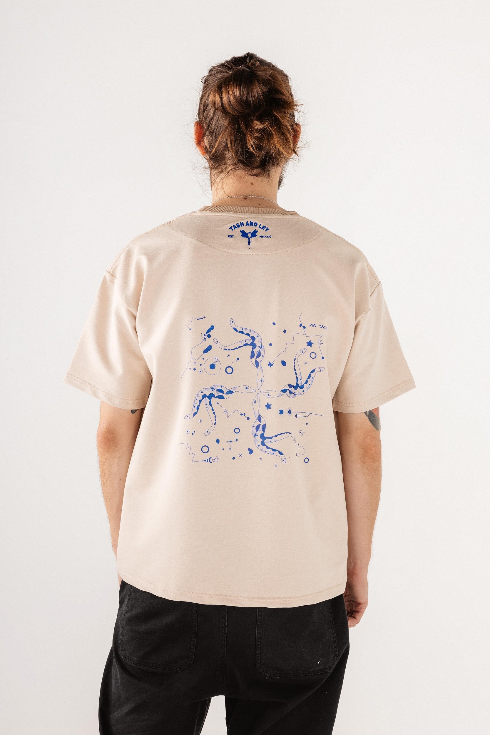 Male model wearing beige top with blue print design on back
