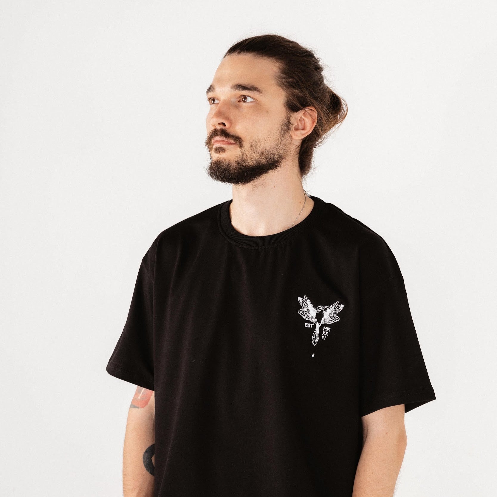 Male model wearing black top with white hummingbird embroidery in front