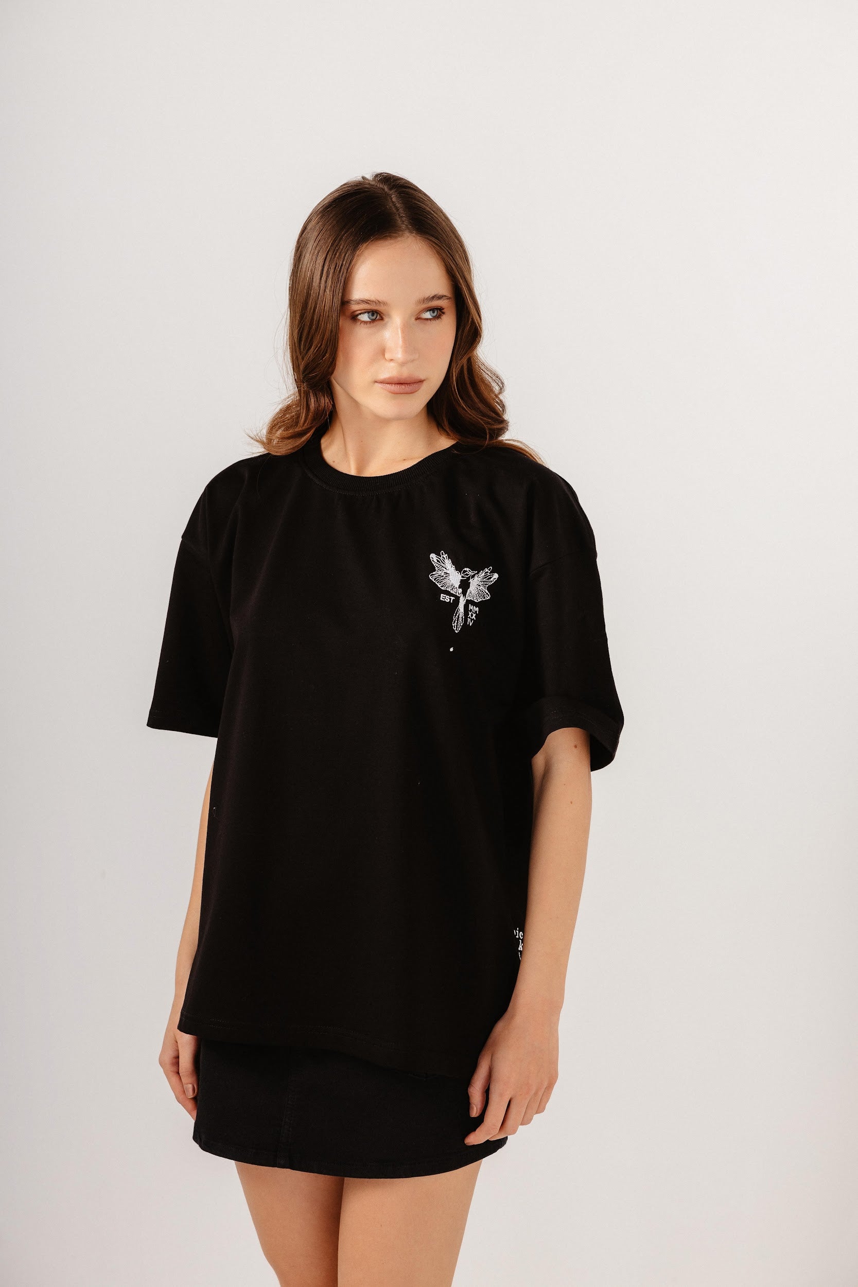Model wearing oversize black top with white embroidery in front