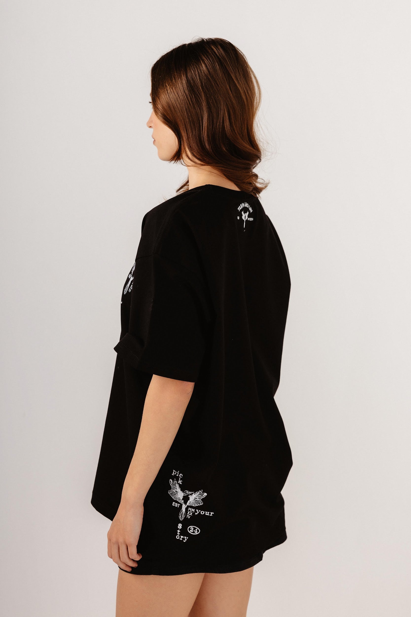 Model wearing oversize black top with white embroidery design n back