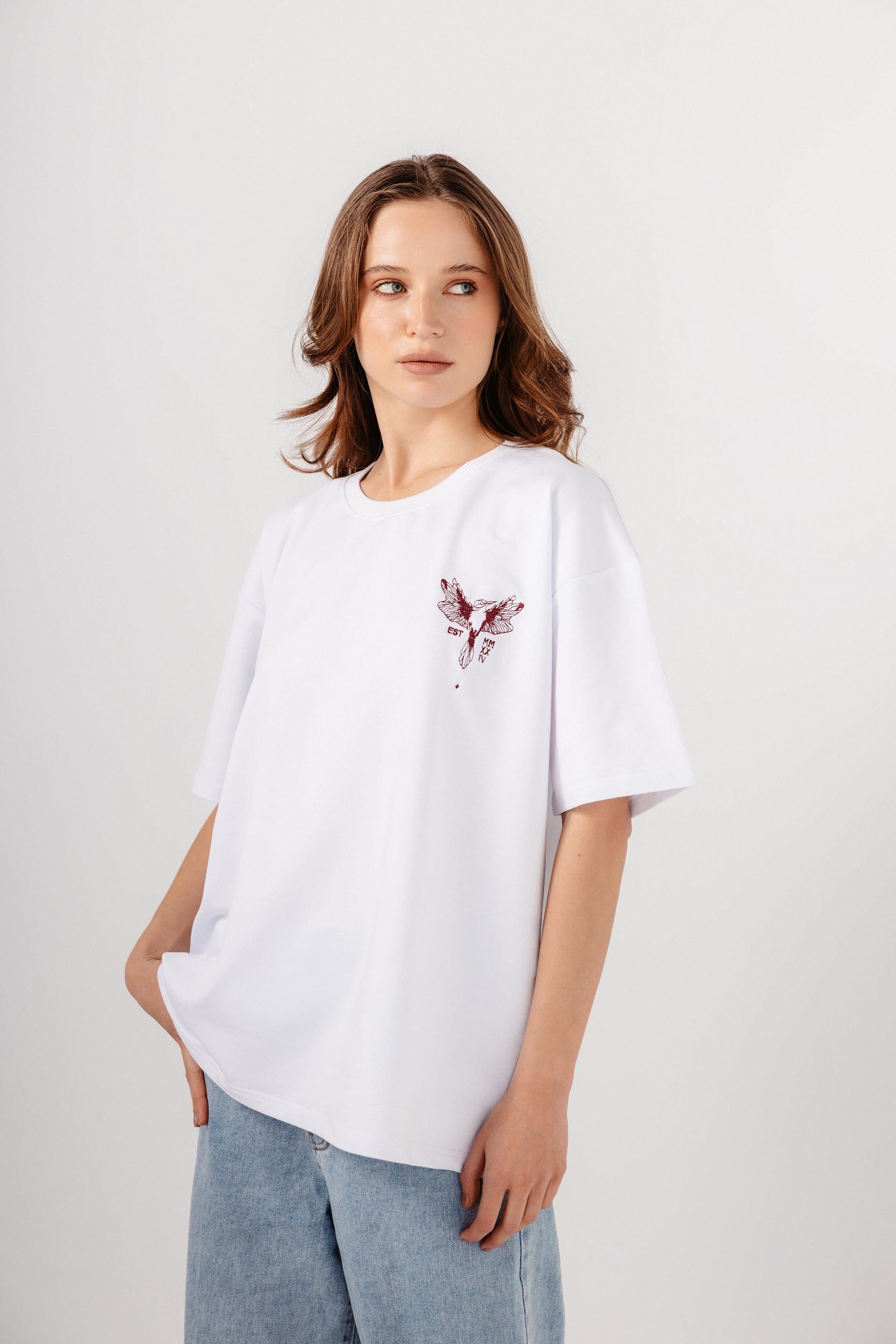 Model wearing oversized white top with dark red embroidery in front