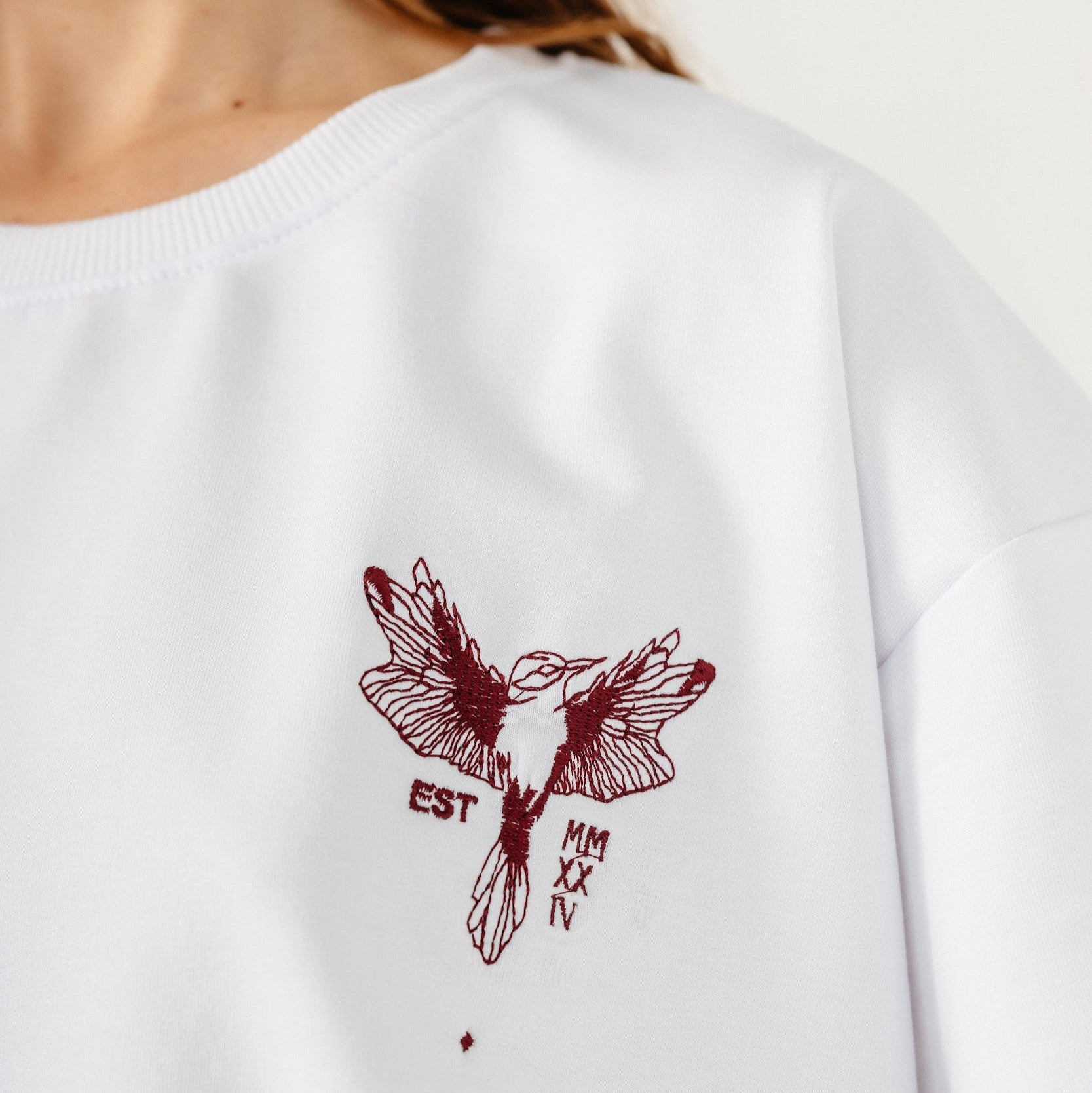 Model wearing white top with dark red hummingbird embroidery in front