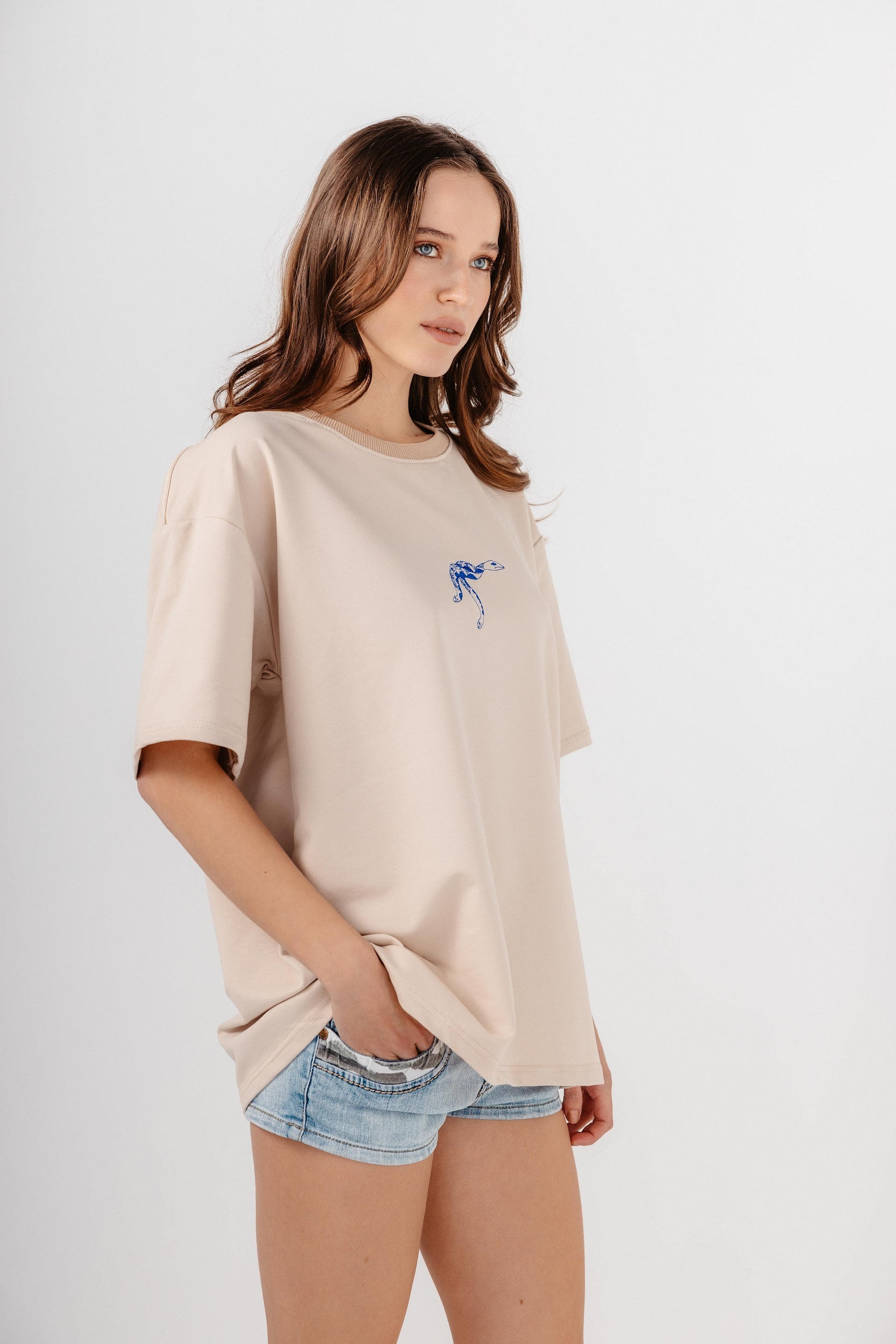 Model wearing oversized beige top with blue embroidery in front