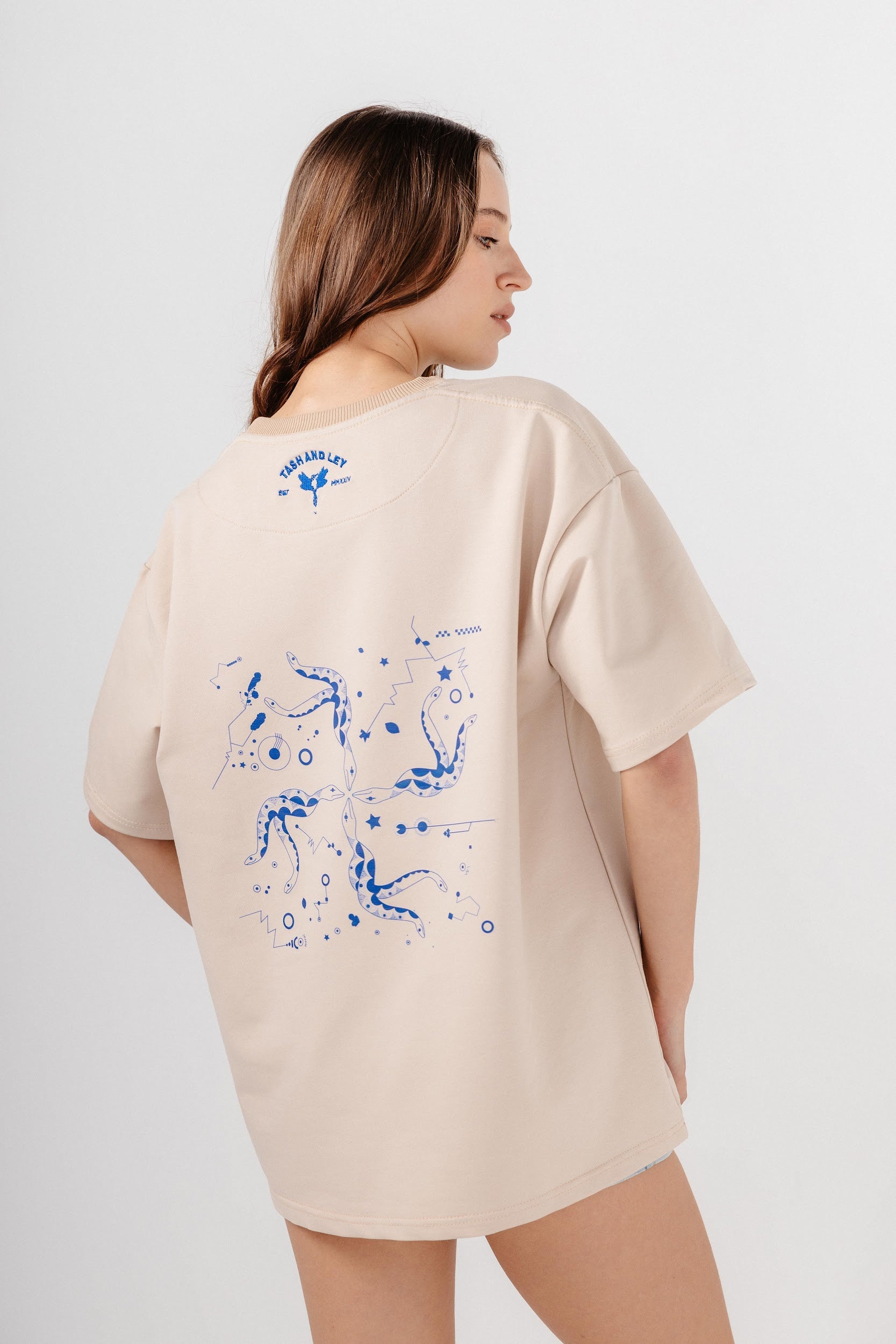 Model wearing oversized beige top with blue print and embroidery on back