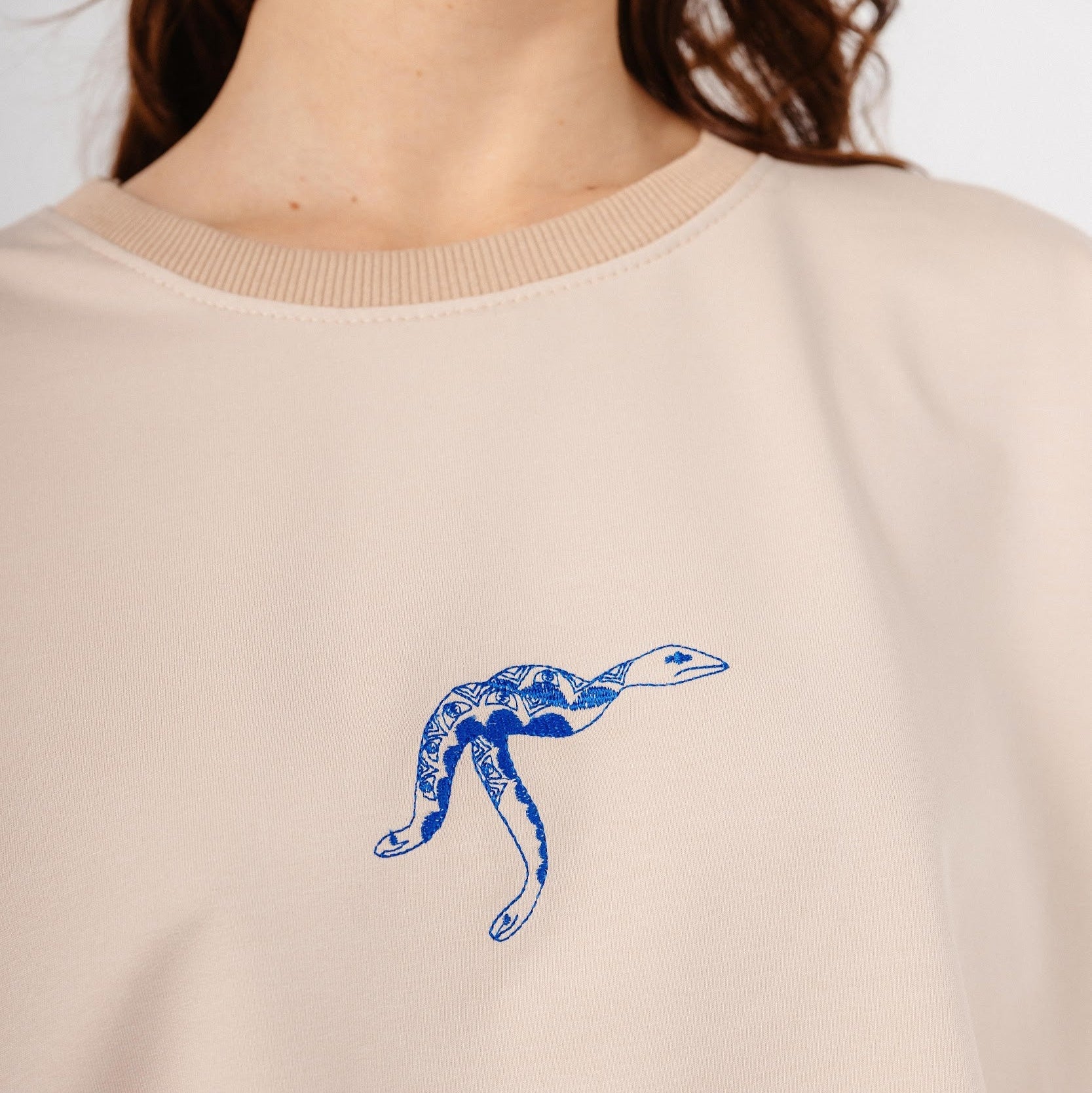 Model wearing beige top with blue snake embroidery