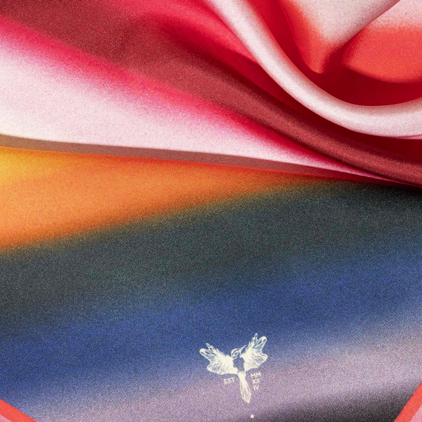 Colorful silk fabric with a multicolor pattern and hummingbird logo in the corner