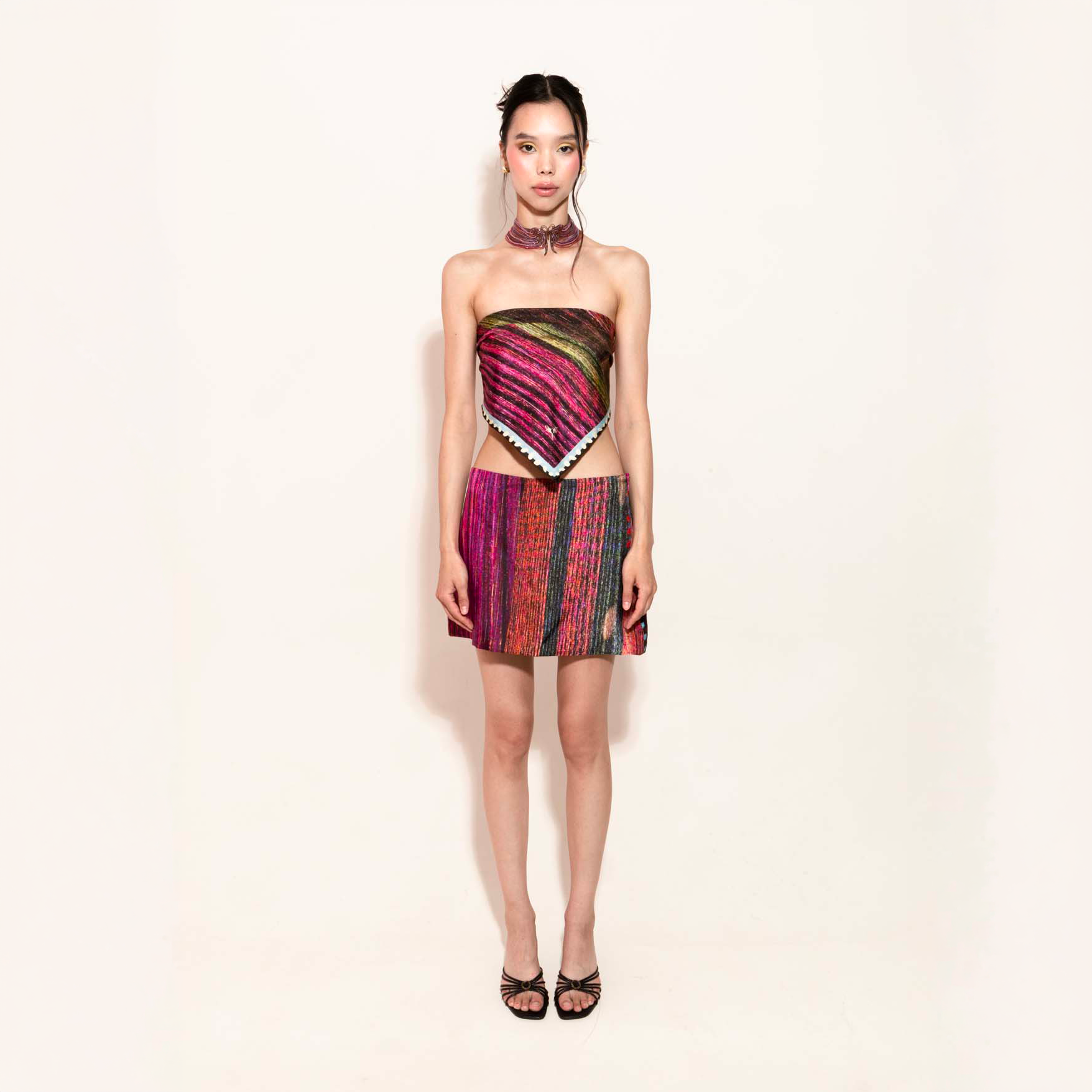 Model wearing a colorful set with a silk scarf as a top and a matching silk skirt on a plain background