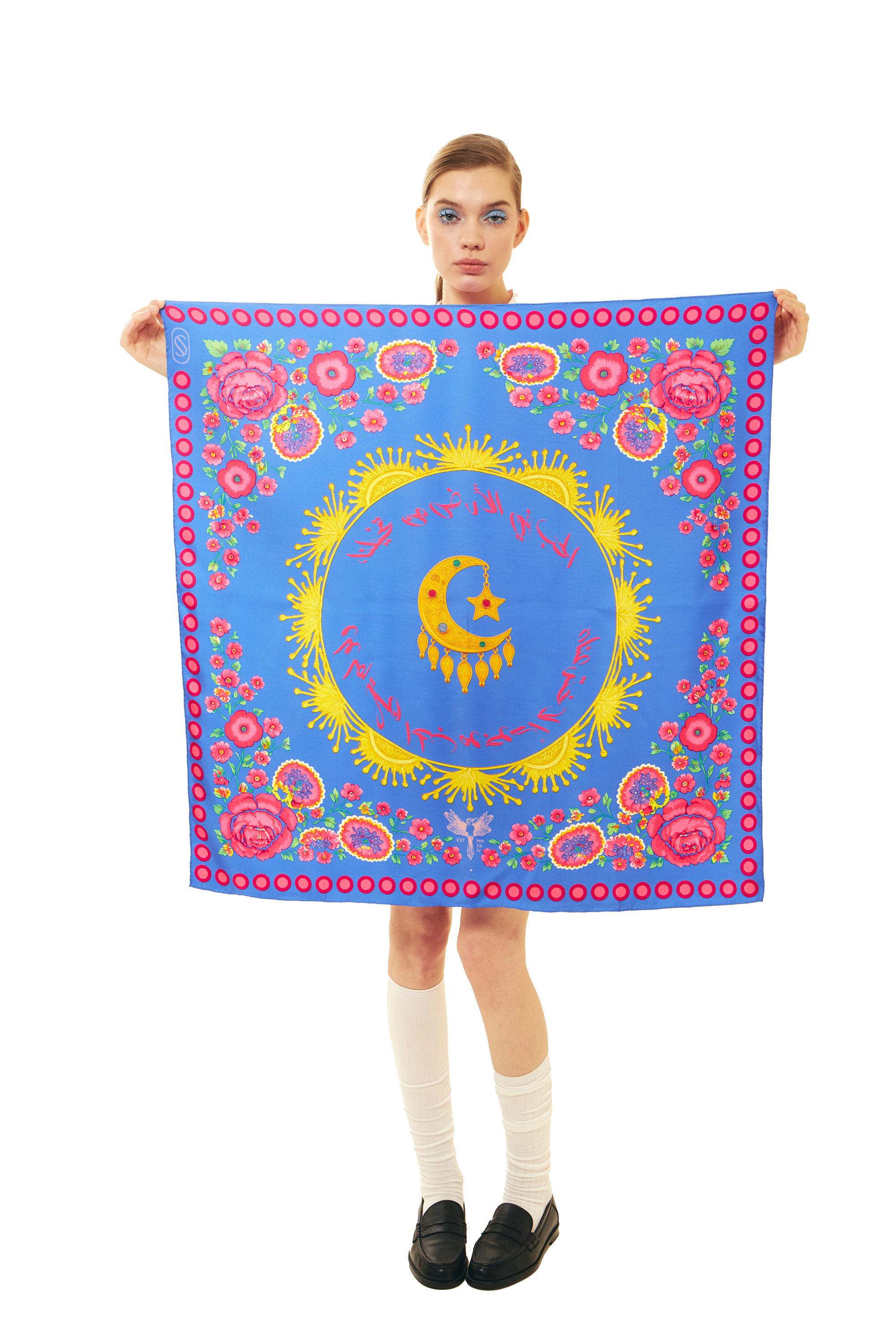 Person holding a blue silk square scarf with pink and gold floral and moon designs on a white background