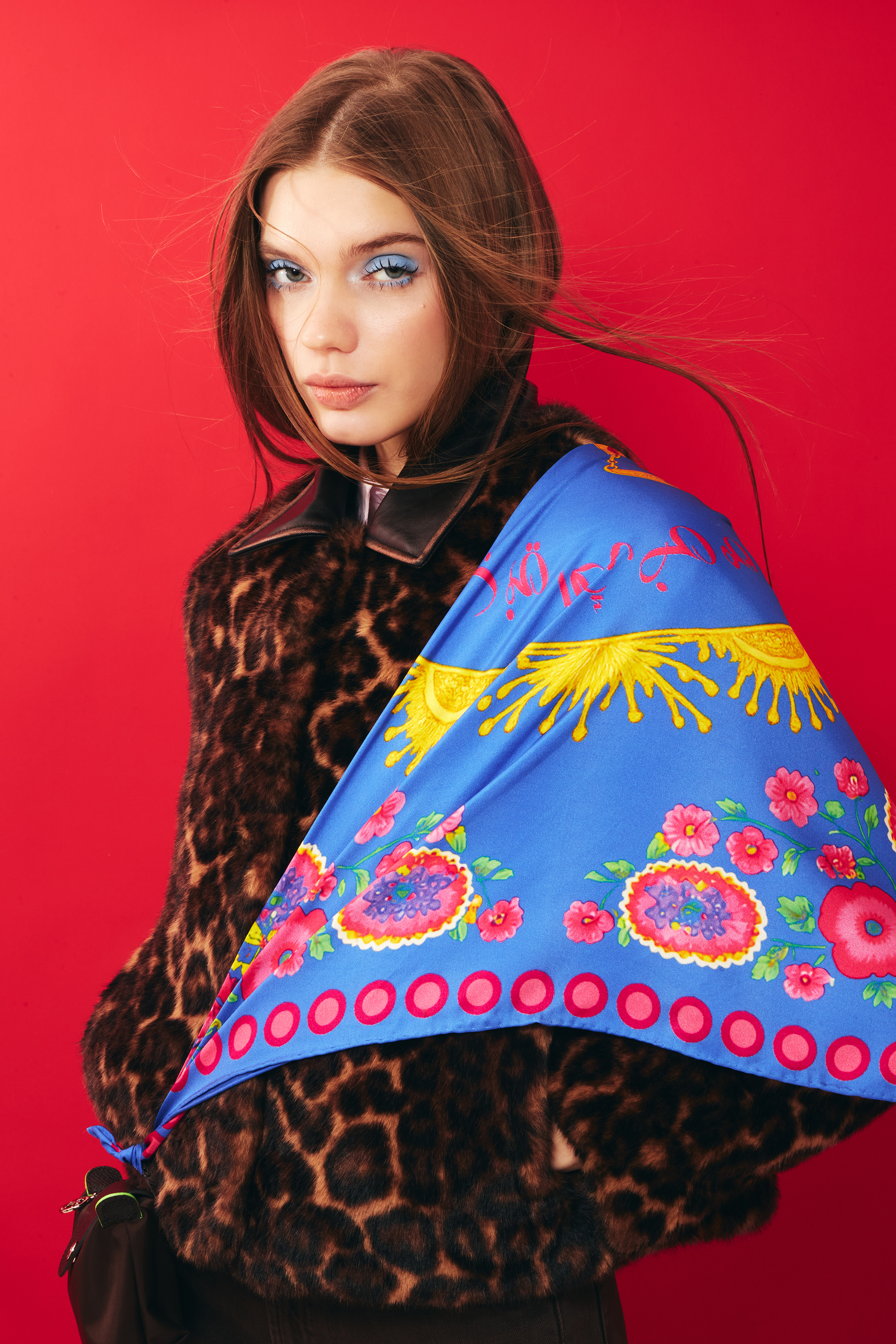 Woman wearing a blue silk scarf with floral patterns around her shoulder as a bag strap