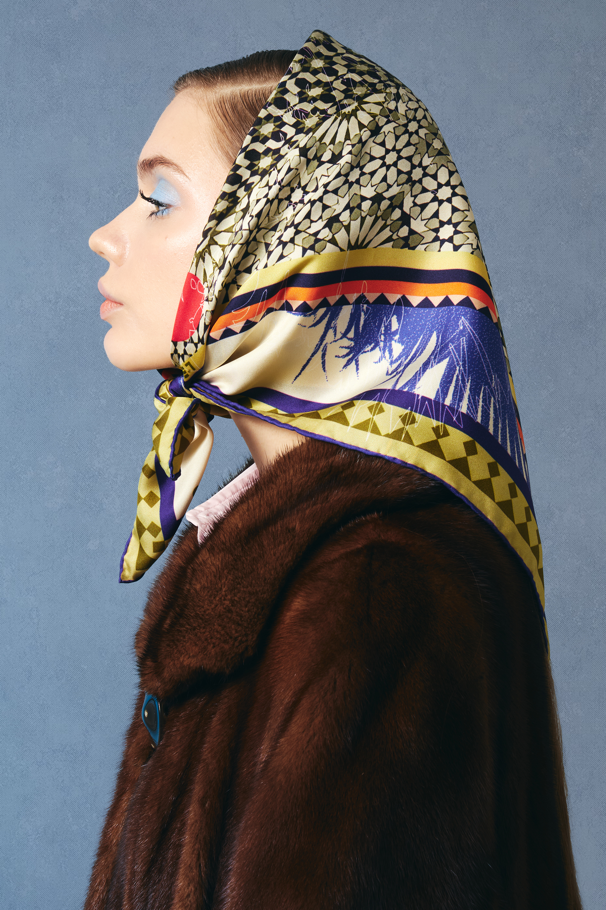Woman wearing a patterned beige silk twill square scarf on her head against a blue vintage background
