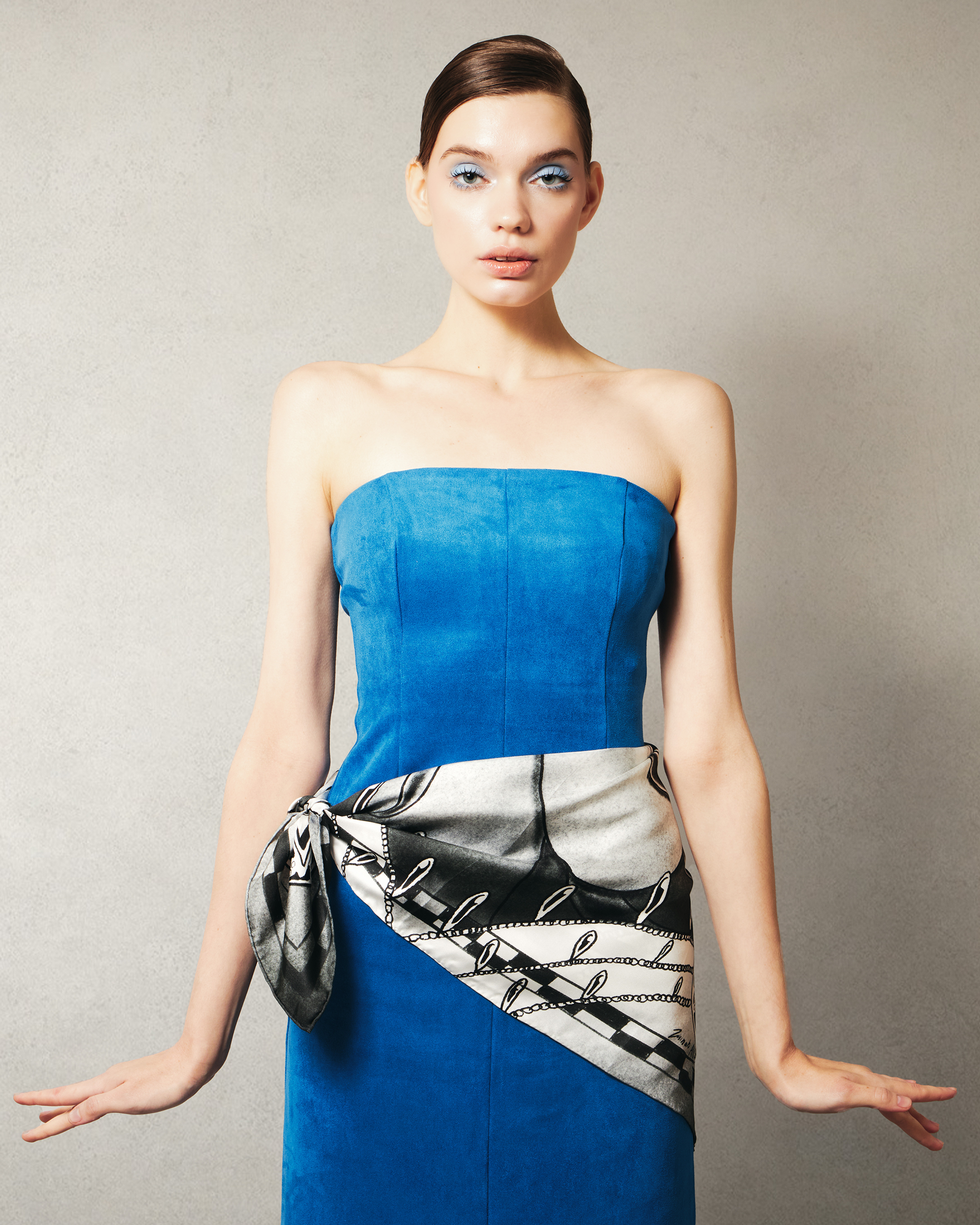 Woman wearing a blue strapless dress with a patterned black and white silk scarf around waist
