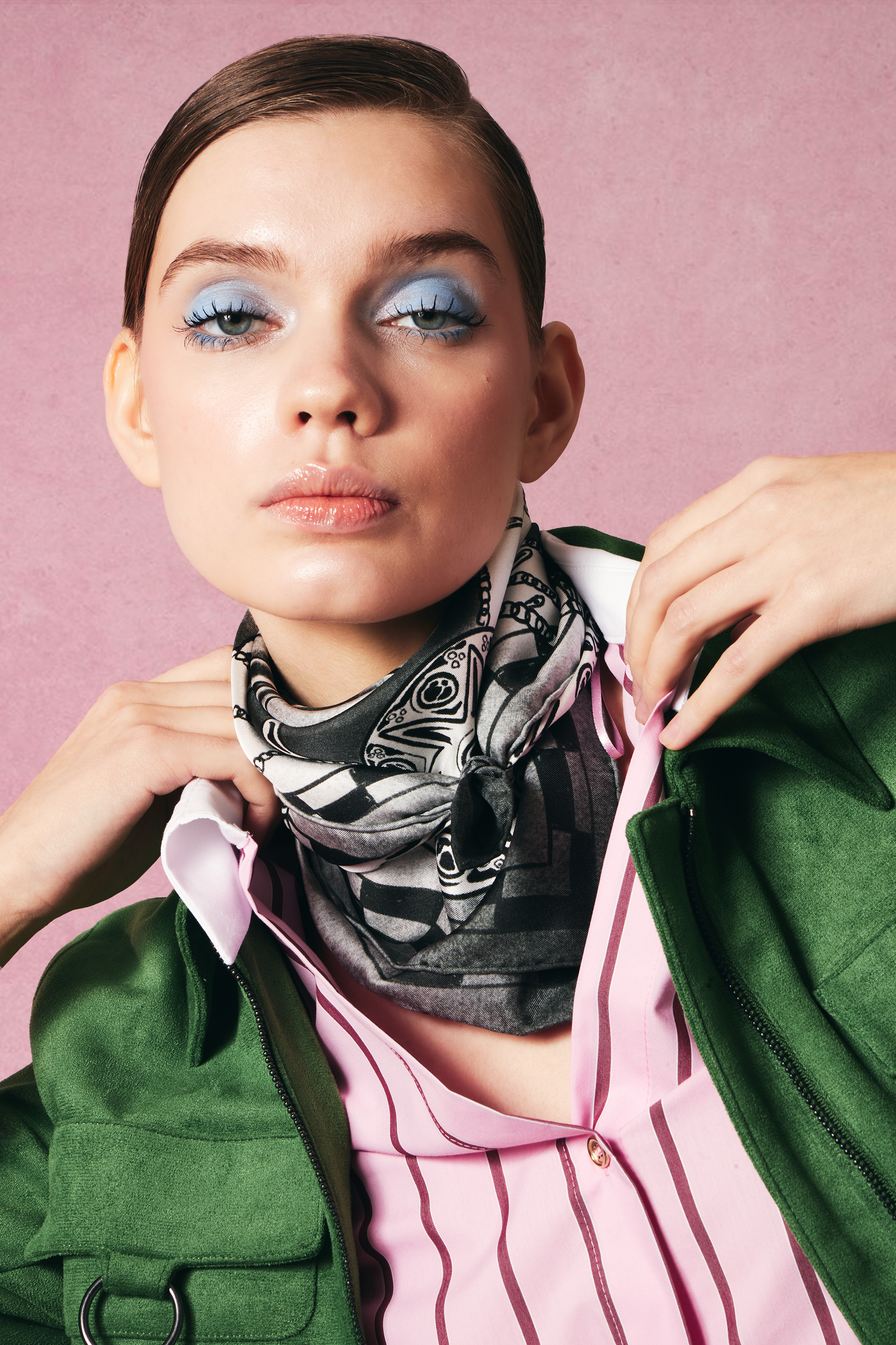 Woman wearing a green jacket and pink shirt with a patterned black and white silk scarf against a pink background