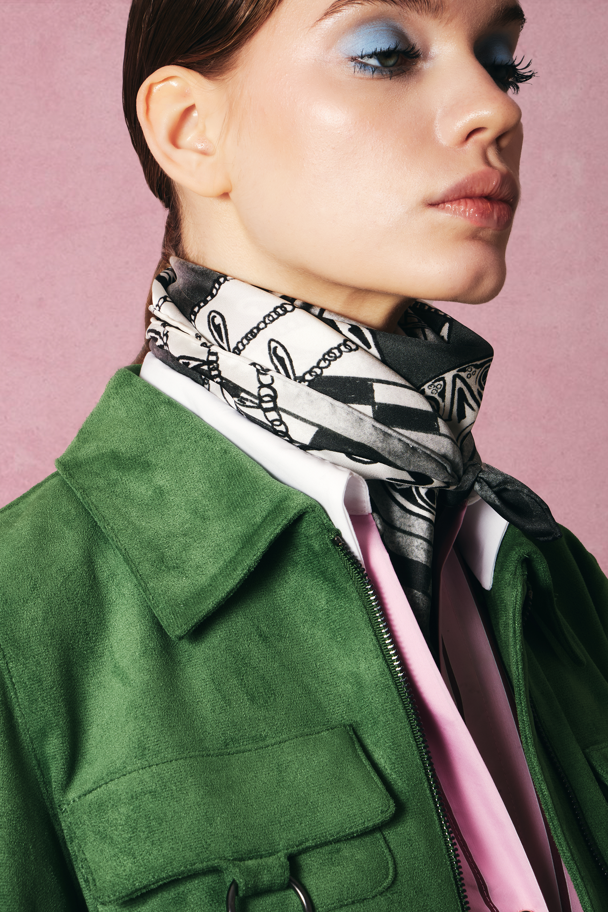 Woman wearing a green jacket and patterned black and white silk square scarf around her neck