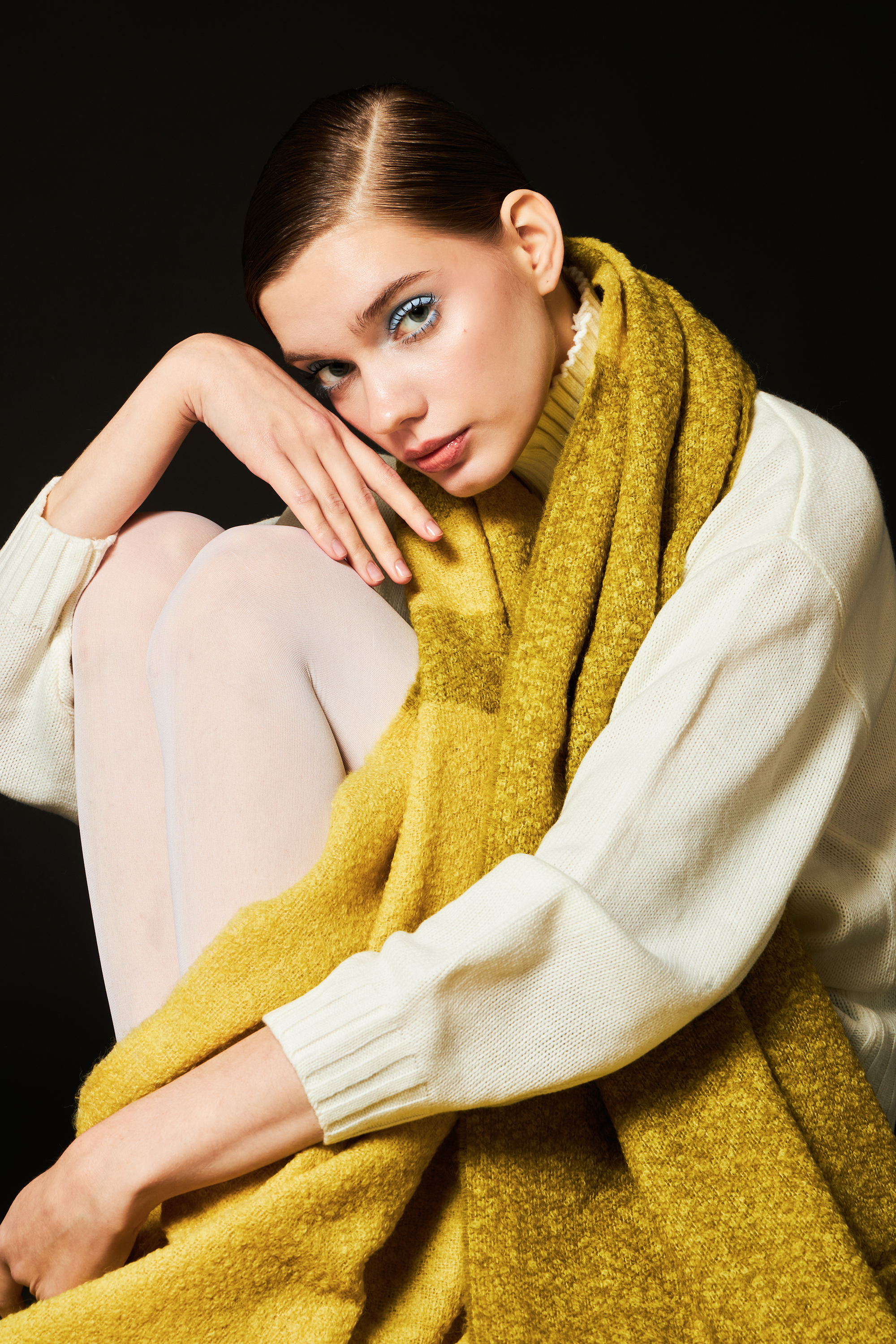 Woman wearing a yellow and green alpaca wool scarf and white sweater against a black background