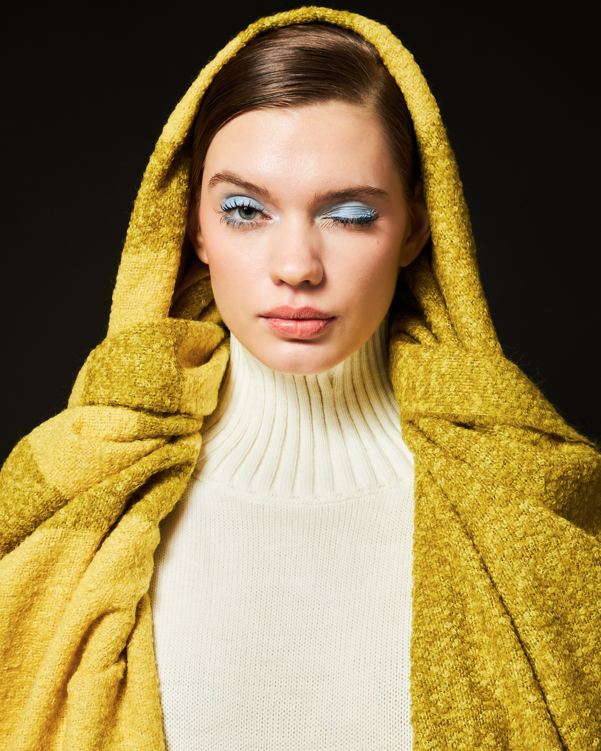 Woman wearing a yellow and green alpaca wool scarf over head against a black background