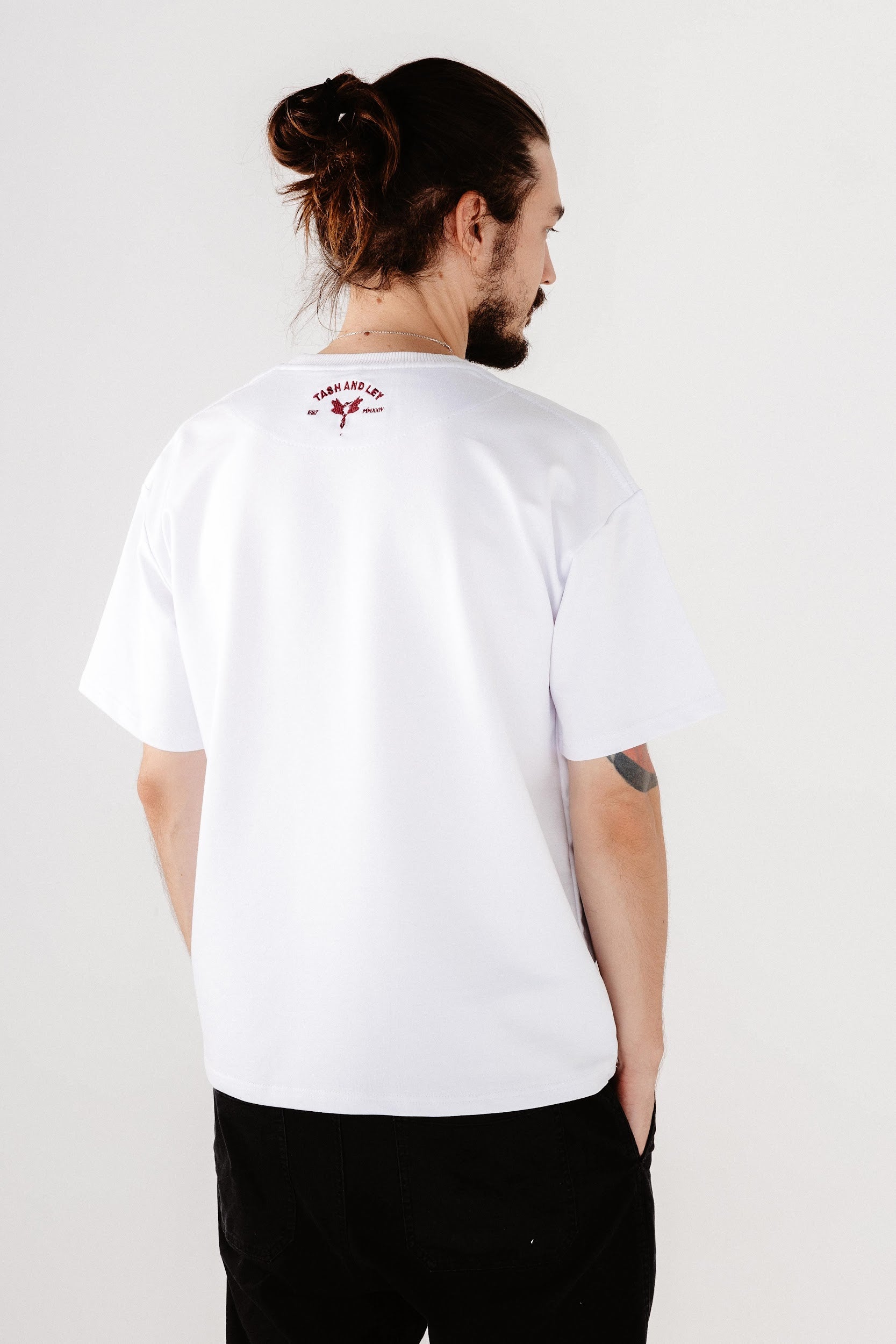 Male model wearing white top in oversized with dark red logo embroidery on back