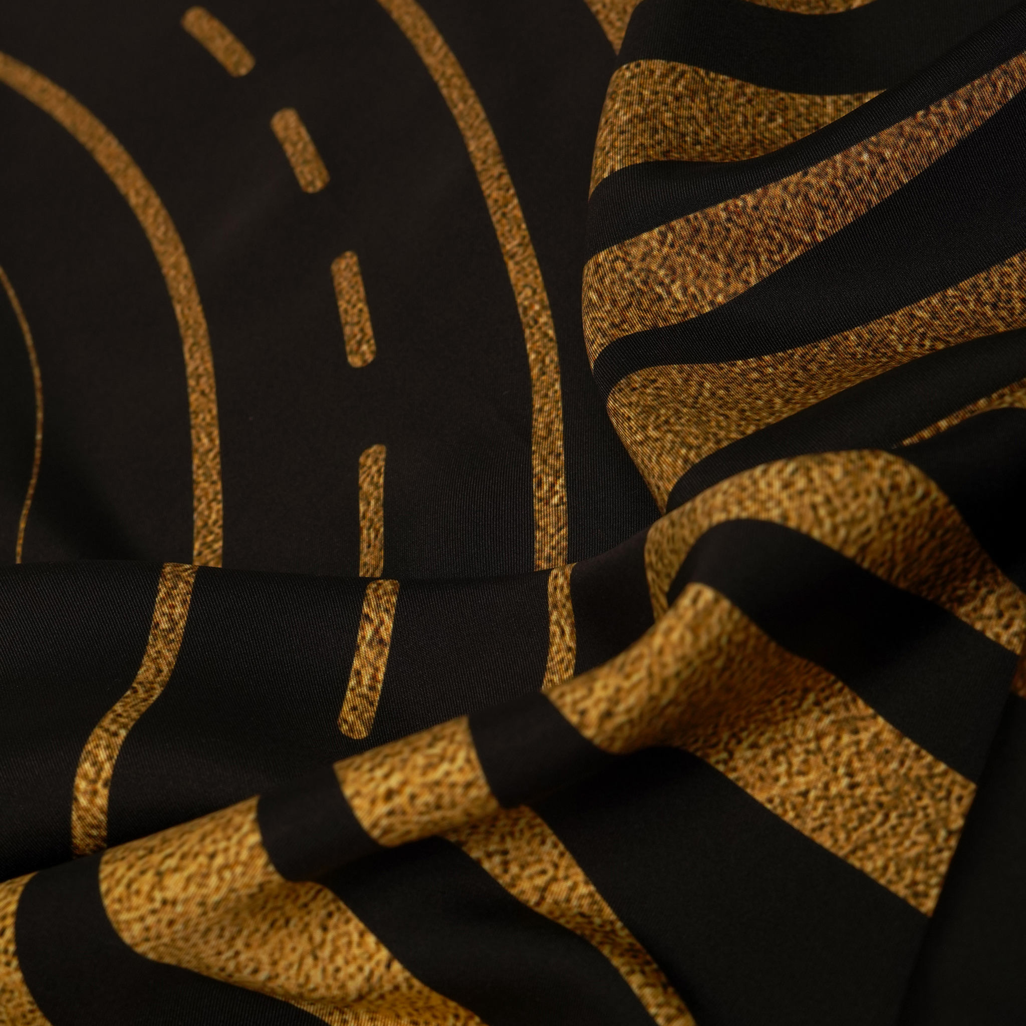 zoom on silk twill fabric in black and gold print with sun motif