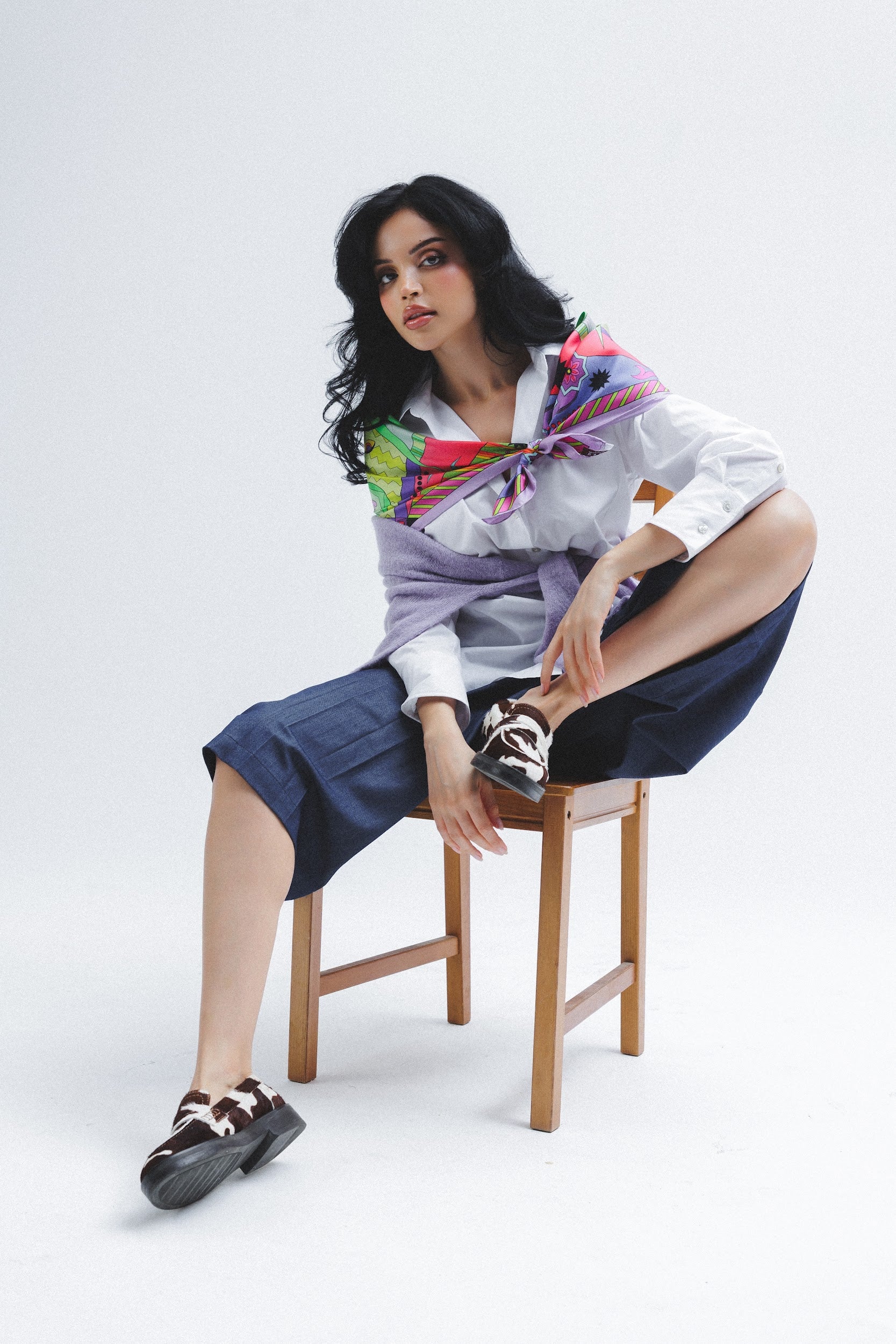 Model sitting on a chair wearing a colorful scarf on her shoulders