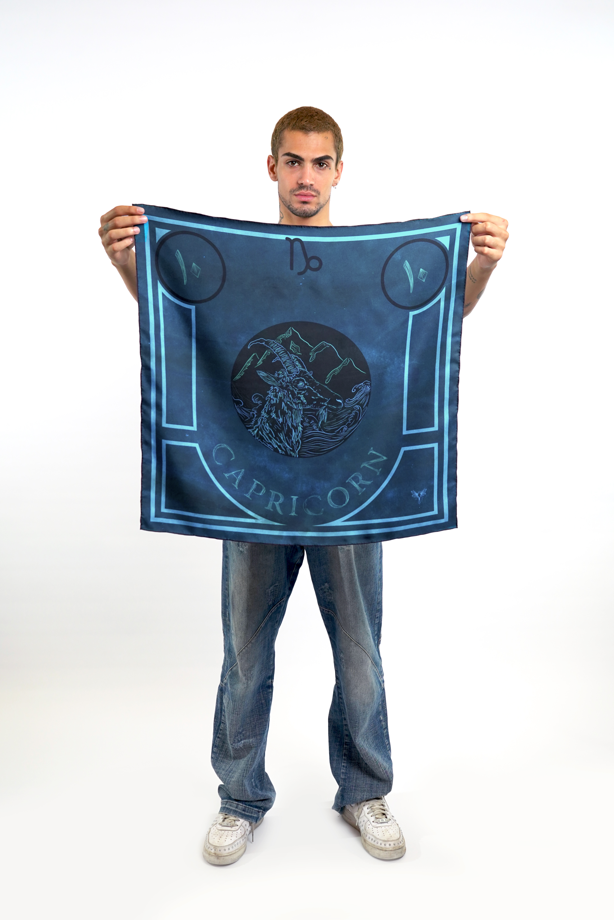 Male model holding silk twill square scarf with capricorn design