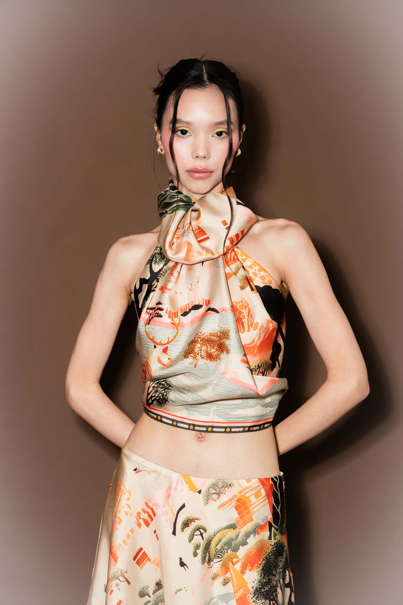 Woman wearing a colorful scarf as a top and skirt against a brown background