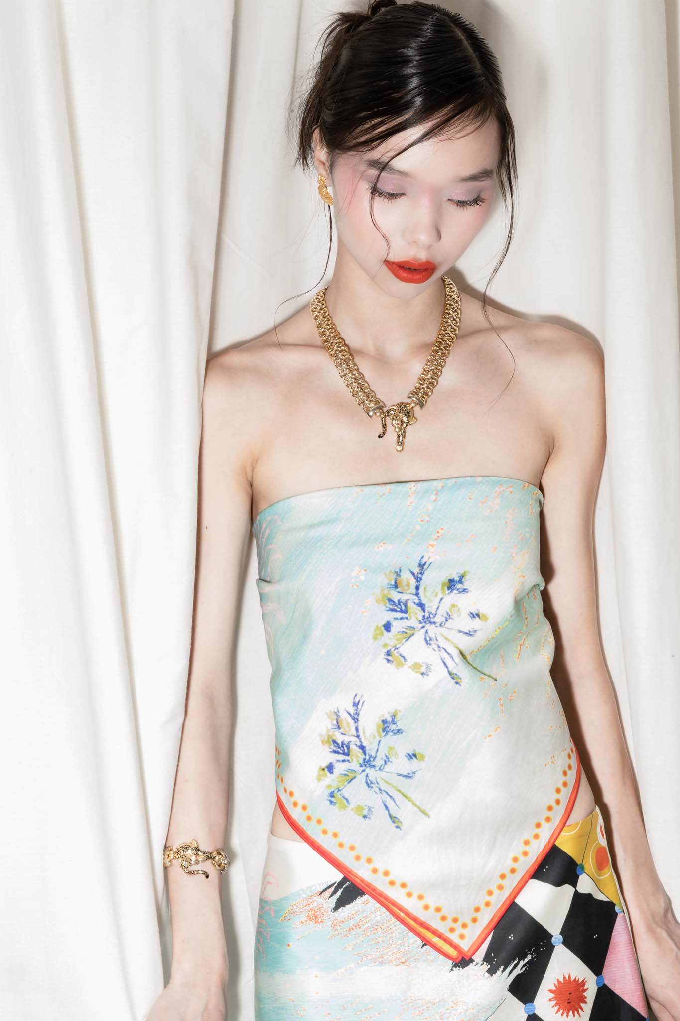 Woman wearing a square scarf as a top with a palm tree beach design against a white curtain background