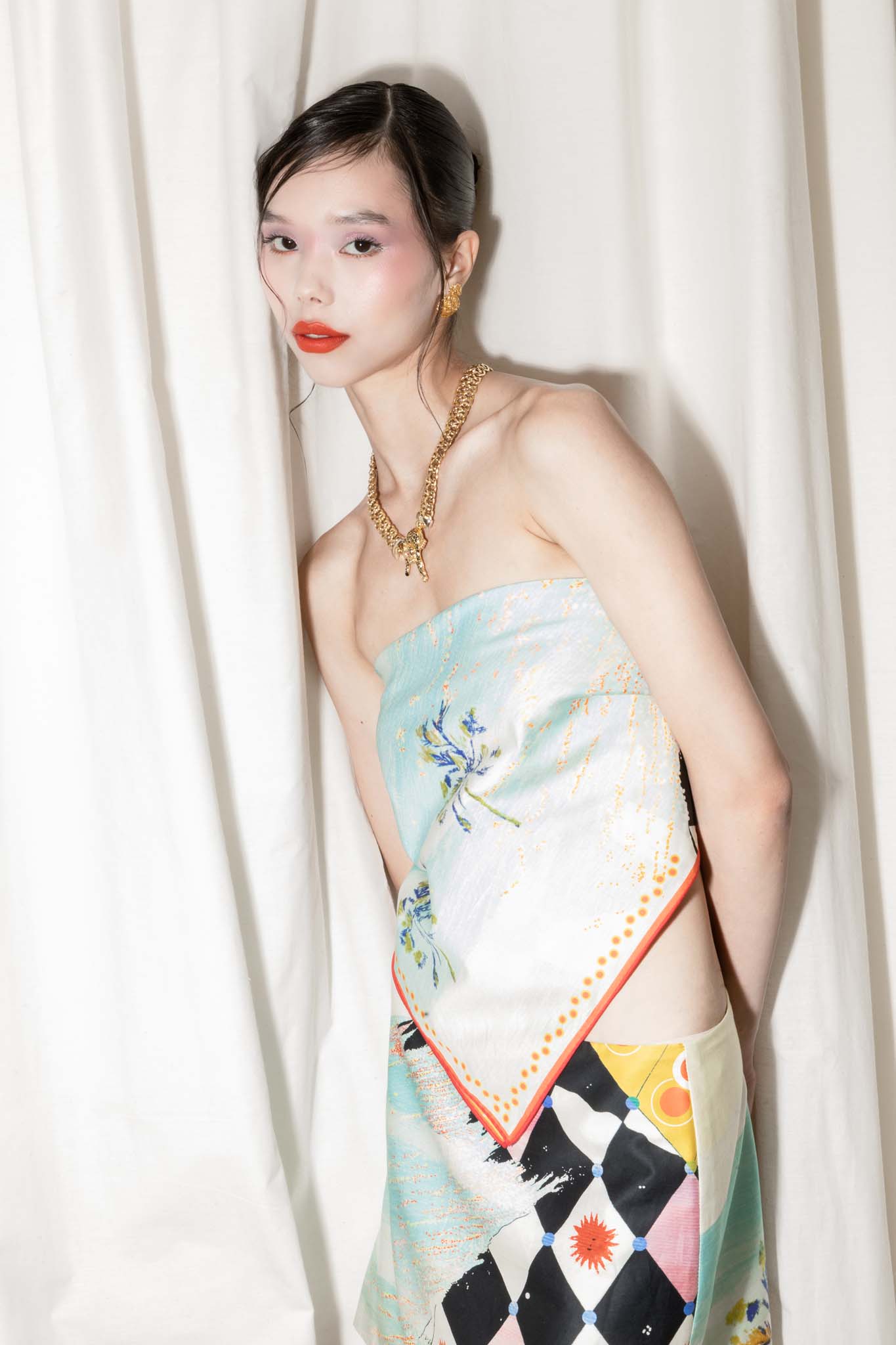 Woman wearing a scarf as a top and a matching skirt with a geometric pattern against a white curtain.