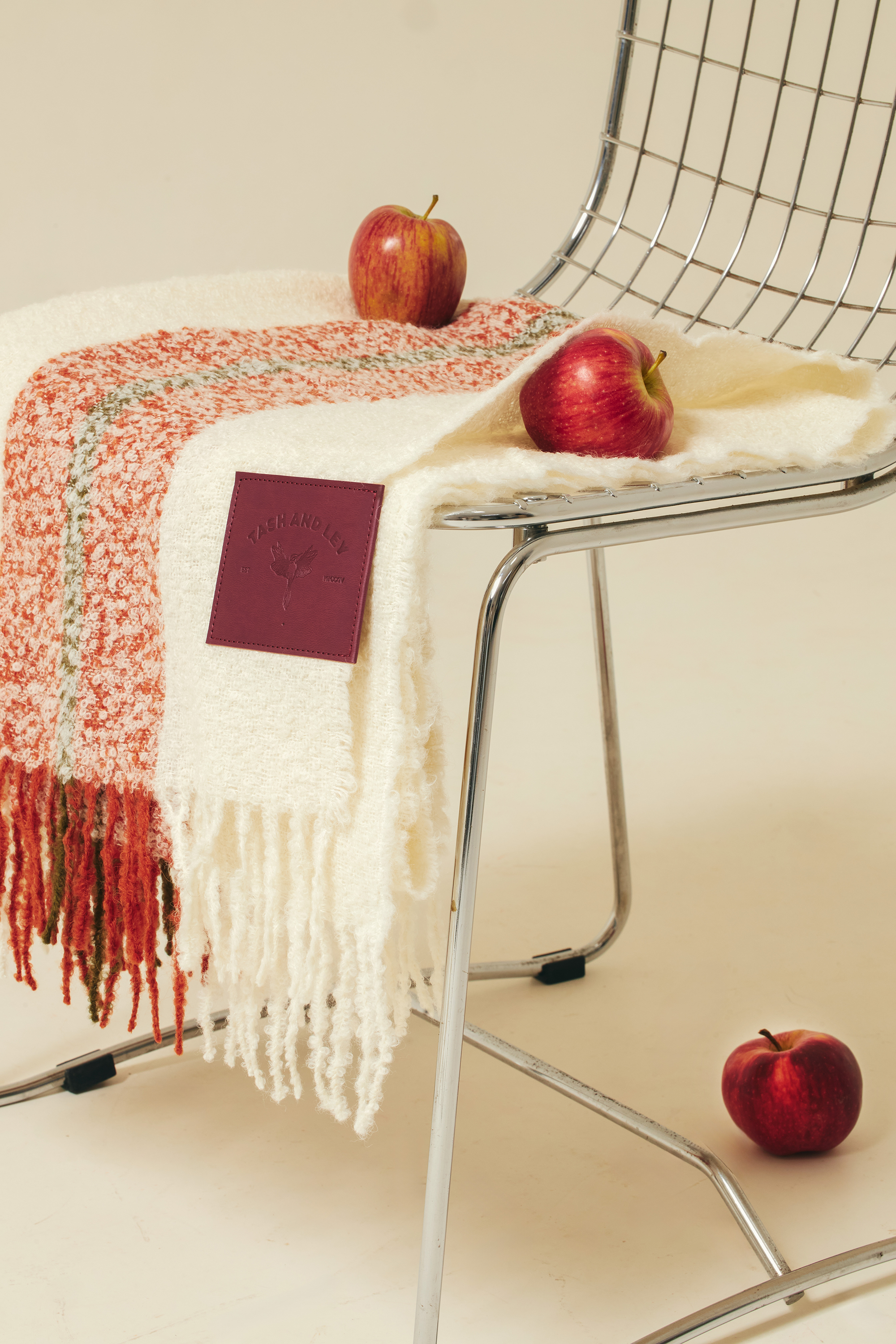 White red-orange and khaki alpaca wool winter scarf with red apples on a metal chair against a beige background
