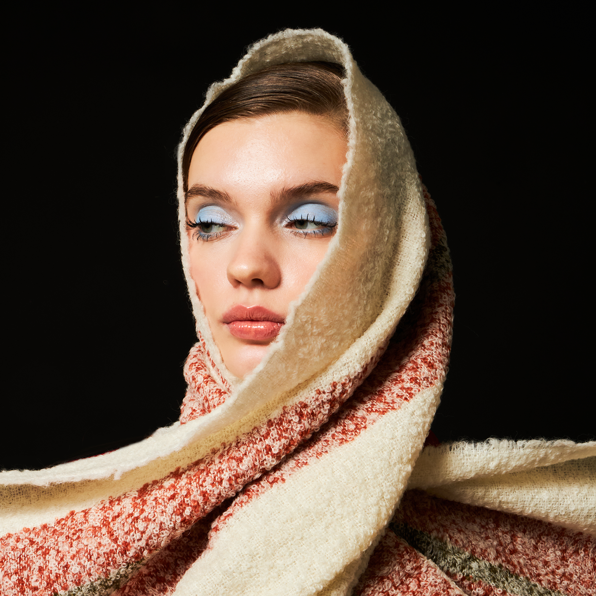 Person wrapped in a white and red striped alpaca wool scarf with a black background